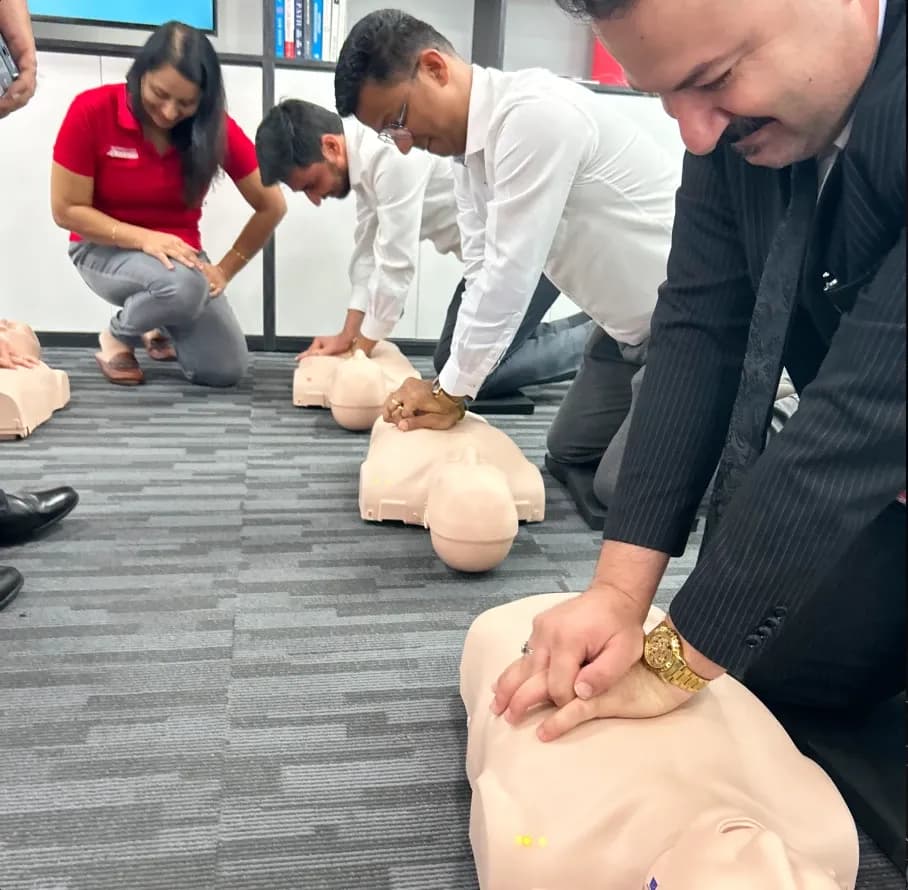 First aid instructor guiding students during a hands-on CPR training session with medical manikins on the floor.