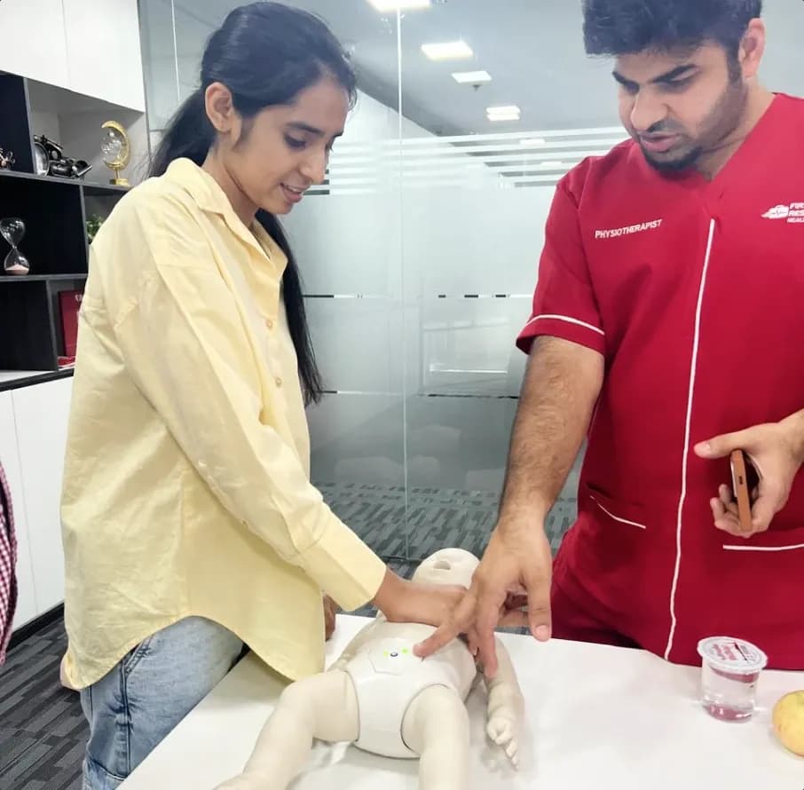 A first aid instructor in a red medical uniform guiding a female student during a hands-on clinical training session.
