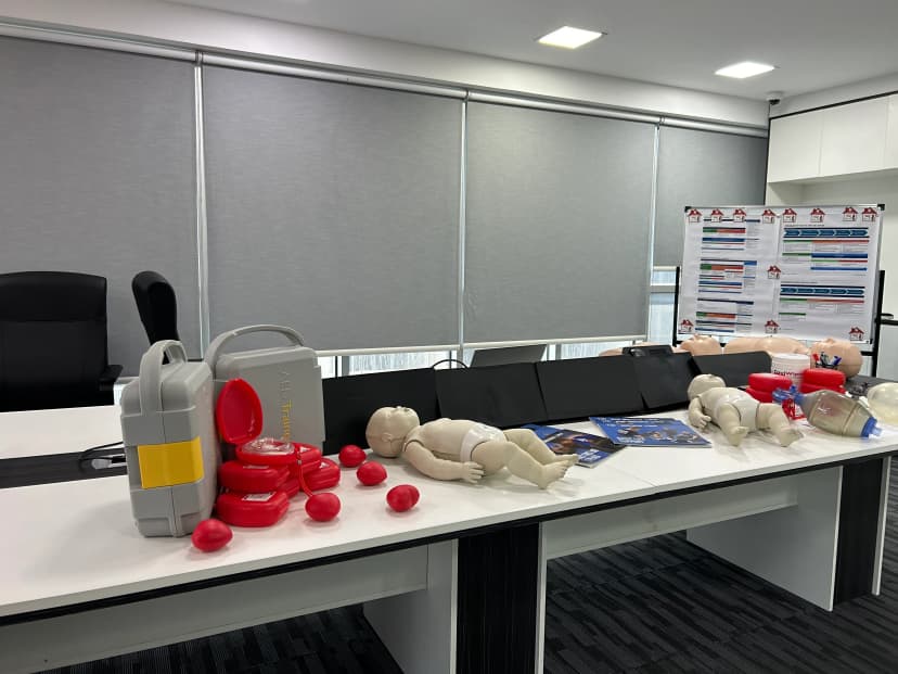 A first aid training classroom setup featuring a medical equipment layout, first aid kit, and CPR manikins arranged on a conference table for a practical certification course.