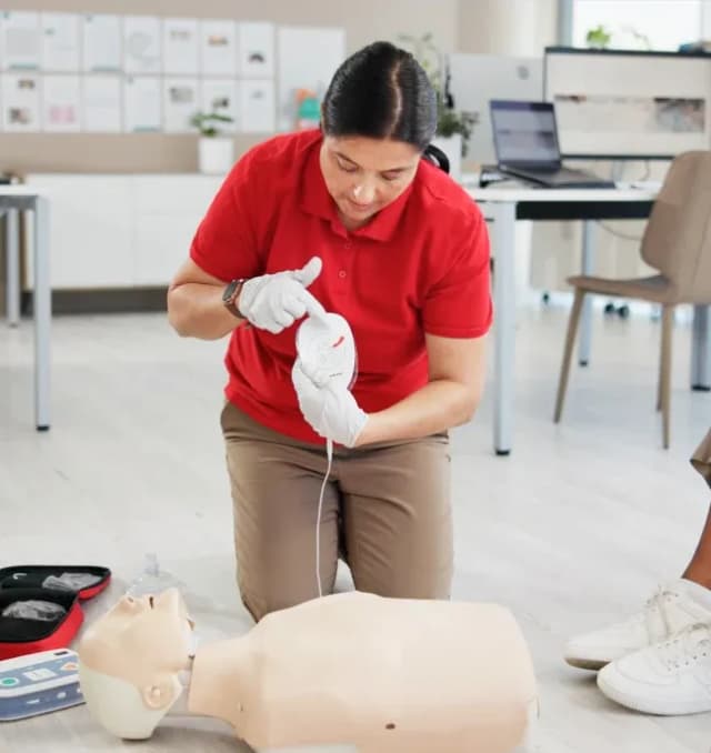 A First Response Healthcare first aid instructor in a red uniform demonstrating wound care and bandaging techniques during a training session.