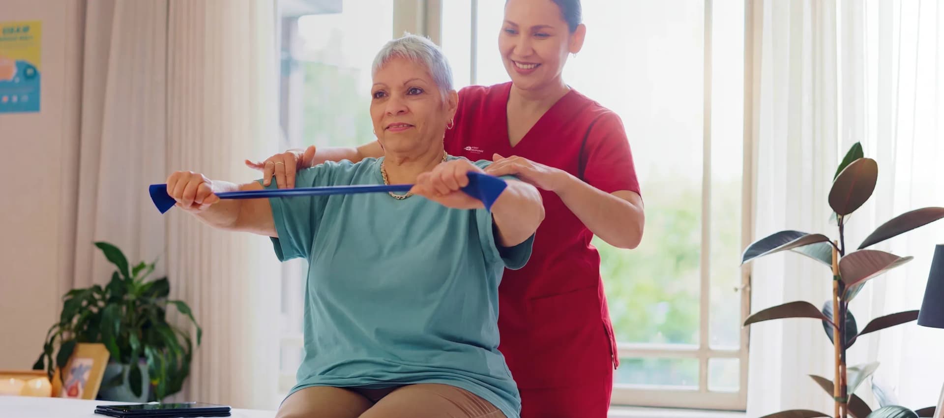 A female physiotherapist assisting an elderly woman with resistance band exercises during an at-home geriatric physiotherapy session by First Response Healthcare in Dubai.