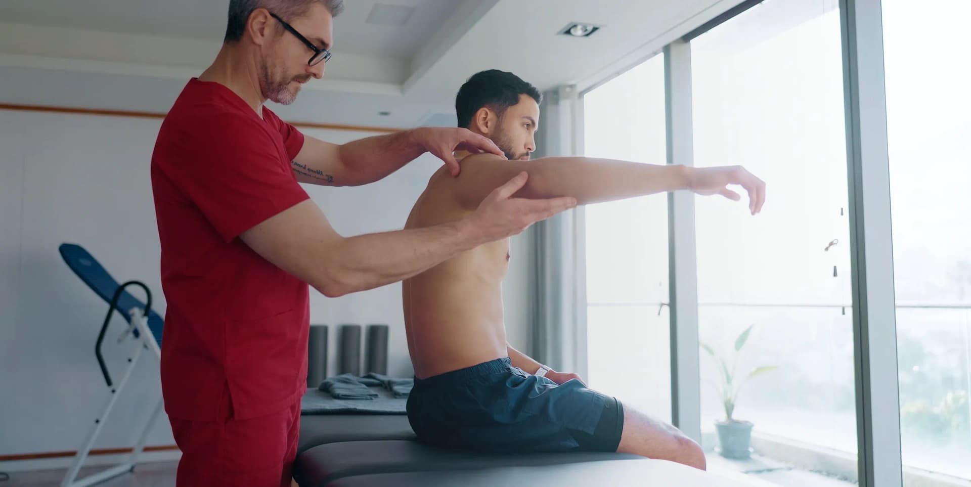DHA-licensed physical therapist explaining frozen shoulder physiotherapy treatments to a patient during an at-home session in Dubai.