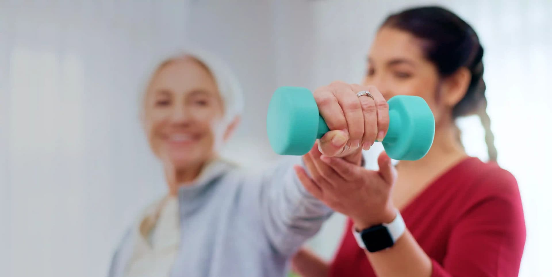 A female physiotherapist in uniform assisting an elderly patient with dumbbell exercises during an at-home cardiorespiratory physiotherapy session by First Response Healthcare in Dubai.