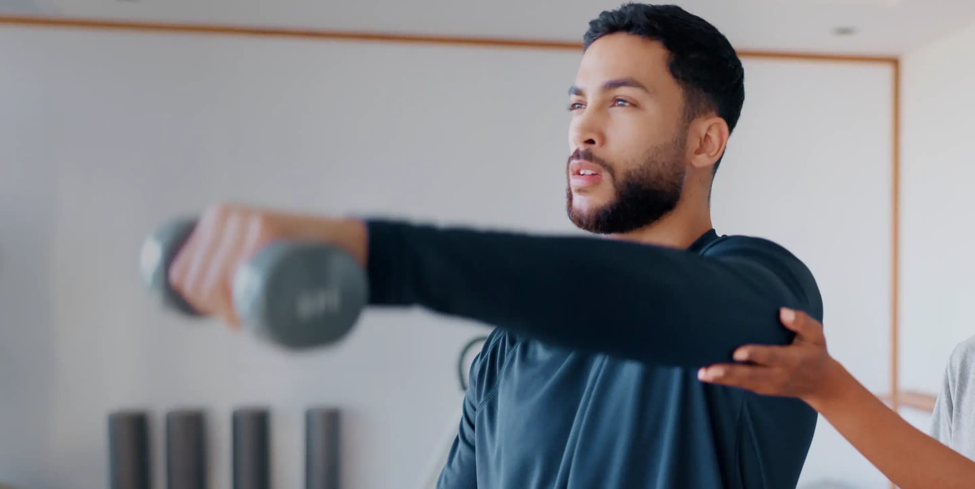 A male patient performing arm resistance exercises with a dumbbell during a home neuro physiotherapy session in Dubai.