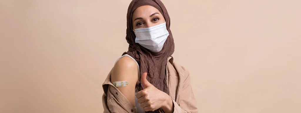 Woman in a hijab-wearing a mask, showing vaccinated arm, symbolizing Umrah vaccination