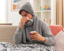 A man sitting on the couch indicating he has a flowing nose due to a cold