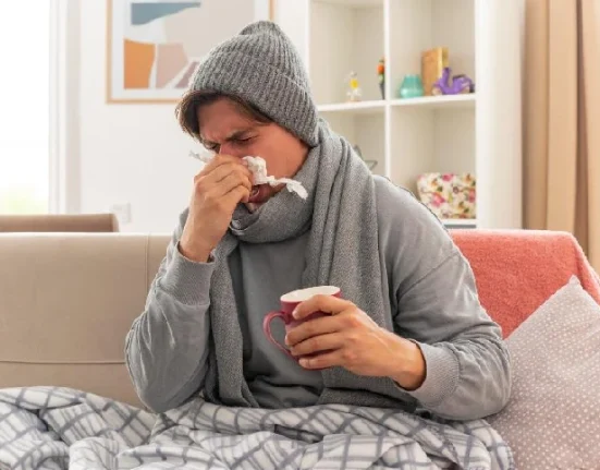 A man sitting on the couch indicating he has a flowing nose due to a cold