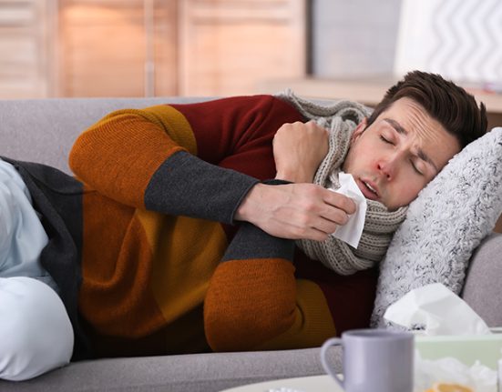 A man lying on the sofa due to a cold and medicines on the table
