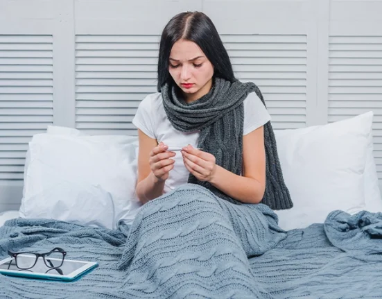 A woman on bed checking body temperature with a thermometer