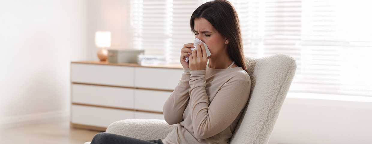 A woman sitting on the couch whipping her nose due to cold