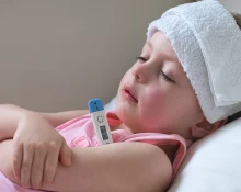 A young child lying in bed with a cold towel on the forehead