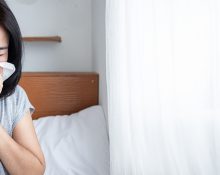 Woman on bed sneezing into tissue due to Sinus infection