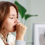 A woman coughing while wrapped in a blanket