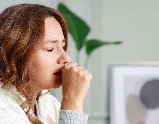 A woman coughing while wrapped in a blanket