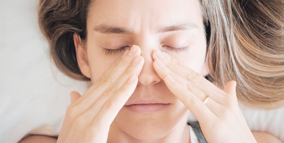 A woman pressing her sinus area due to chronic sinusitis discomfort