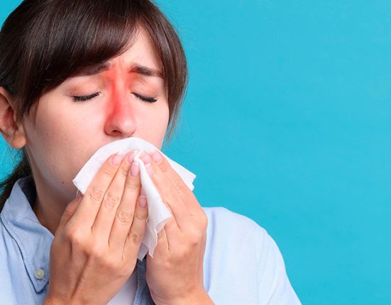 A woman with inflamed sinus areas blowing her nose, indicating chronic sinusitis